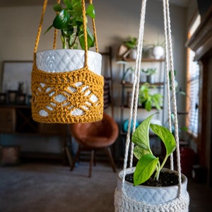 May include: Two macrame plant hangers with white ceramic pots and green plants. The hanger on the left is yellow and the hanger on the right is white.