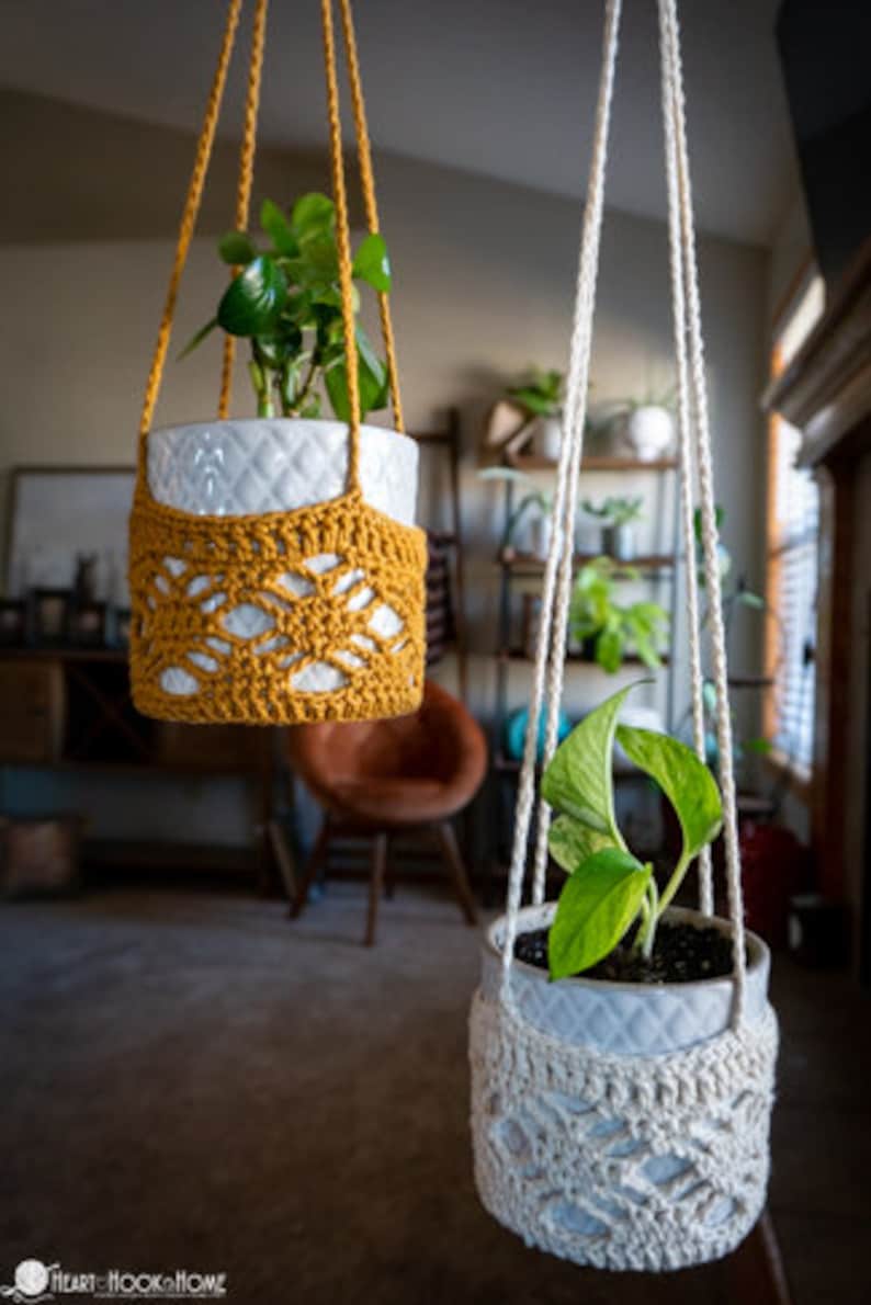 May include: Two macrame plant hangers with white ceramic pots and green plants. The hanger on the left is yellow and the hanger on the right is white.