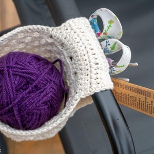 May include: A crocheted yarn holder with a purple ball of yarn inside. The holder is attached to a black metal bar with a pair of scissors and a ruler.