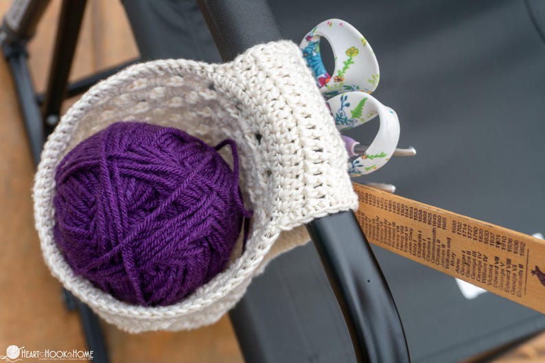 May include: A crocheted yarn holder with a purple ball of yarn inside. The holder is attached to a black metal bar with a pair of scissors and a ruler.