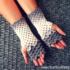 May include: A pair of crocheted fingerless gloves with a gradient colour pattern. The gloves are white and grey and have a scale-like design on the fingertips.