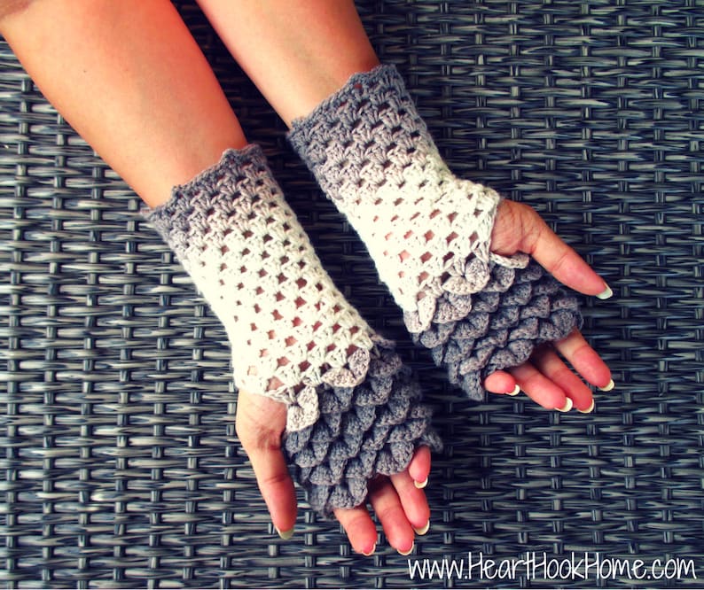 May include: A pair of crocheted fingerless gloves with a gradient colour pattern. The gloves are white and grey and have a scale-like design on the fingertips.