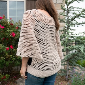 May include: A beige crochet top with a loose, open-weave design. The top has a wide, rounded neckline and long, flowing sleeves.
