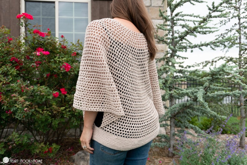 May include: A beige crochet top with a loose, open-weave design. The top has a wide, rounded neckline and long, flowing sleeves.