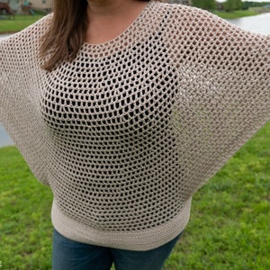 May include: A beige crochet top with a loose, open-weave design. The top has a round neckline and long, wide sleeves.