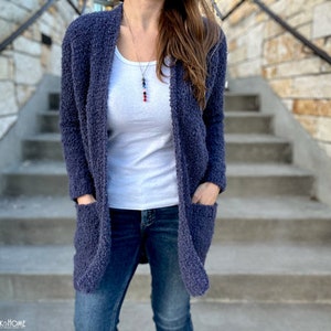 May include: A dark blue cardigan with pockets and a long, open front. The cardigan is made of a soft, fuzzy material and is worn over a white t-shirt and blue jeans.