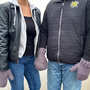 May include: Two people wearing matching purple knitted mittens. The person on the left is wearing a black leather jacket and blue jeans. The person on the right is wearing a black vest and blue jeans.
