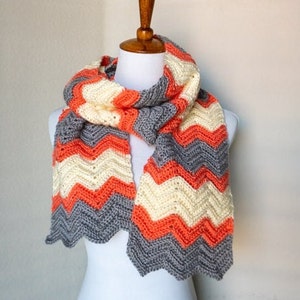 May include: A crocheted scarf with a chevron pattern in shades of gray, orange, and cream.