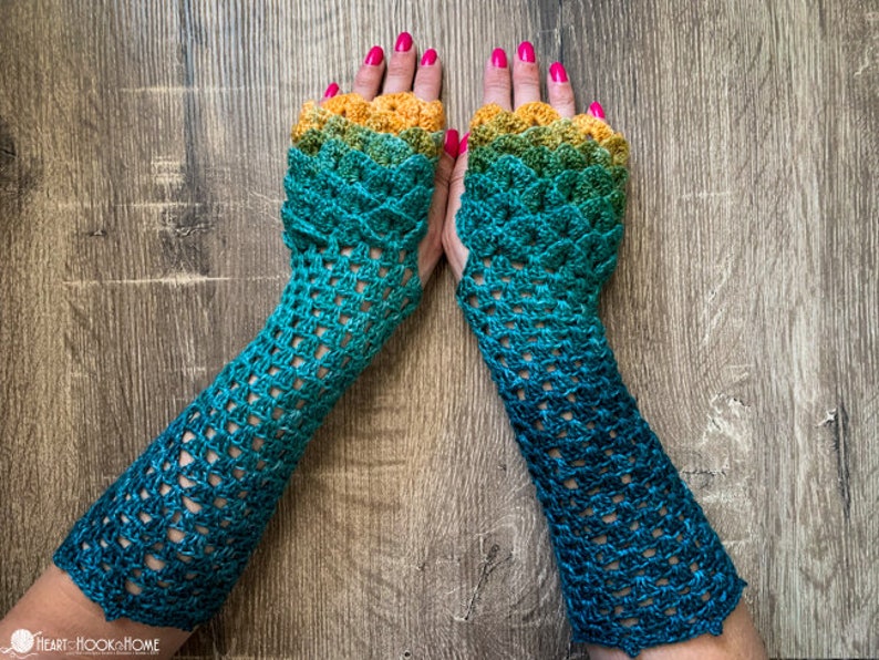 May include: A pair of crocheted fingerless gloves with a gradient colour pattern, transitioning from yellow to green to blue. The gloves have a lacy design and are made with a fine yarn.