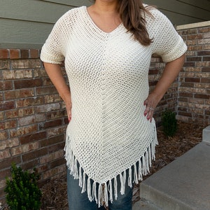 Puede incluir: Un top blanco de crochet con cuello en V y ribete de flecos. El top es holgado y tiene mangas cortas.