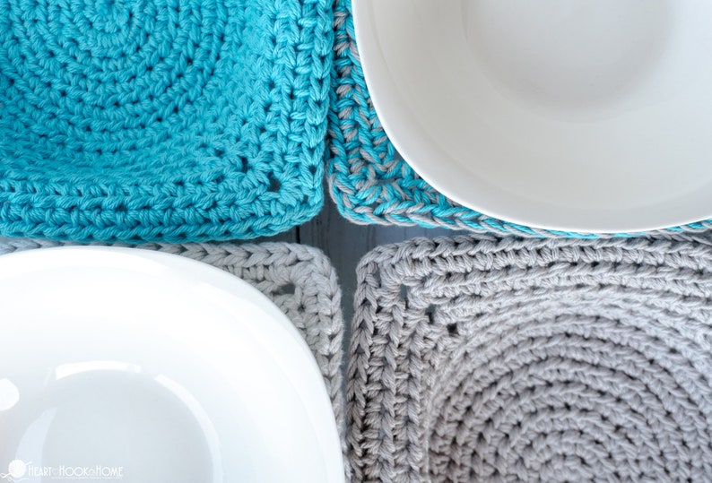 May include: Two crocheted square coasters in gray and turquoise blue, with white bowls on top. The coasters are made with a simple stitch pattern and have a slightly textured surface.