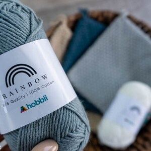 May include: A skein of light blue cotton yarn labelled "Rainbow 8/6 Quality | 100% Cotton" with the hobbii logo.