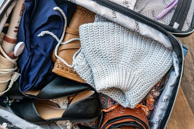 Puede incluir: Maleta abierta llena de art&iacute;culos de viaje. Incluye un su&eacute;ter de ganchillo gris claro, una blusa azul marino, bailarinas negras, una cartera de cuero marr&oacute;n y un secador de pelo. La maleta est&aacute; forrada con una tela estampada.