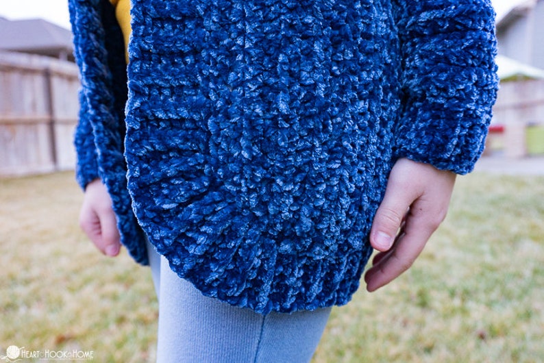 May include: A close-up of a blue fuzzy cardigan with a soft, textured fabric. The cardigan is open in the front and the sleeves are long.