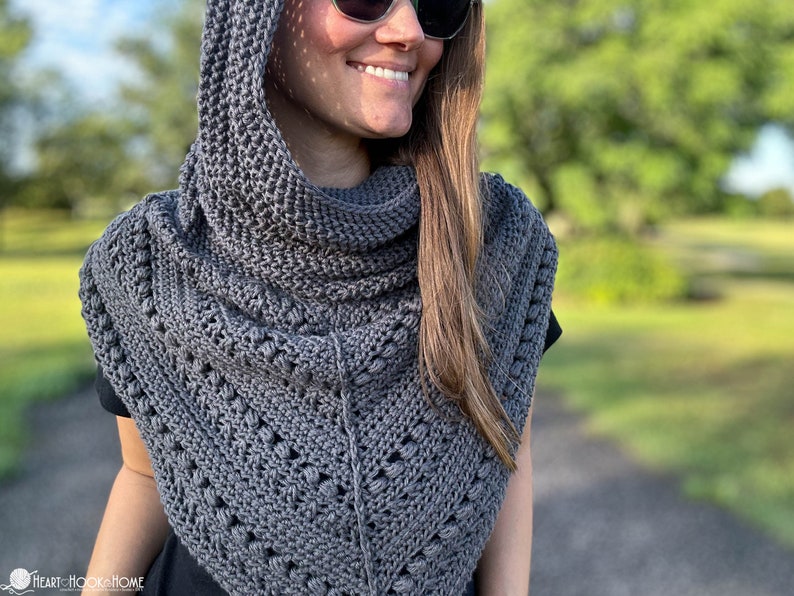 May include: A gray hooded cowl with a crocheted design. The cowl is worn by a person with long brown hair and sunglasses.