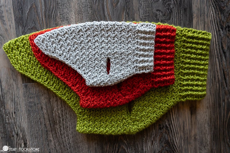 May include: Three crocheted dog sweaters in green, red, and gray. The sweaters are layered on top of each other, with the green sweater on the bottom, the red sweater in the middle, and the gray sweater on top.