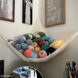 May include: A white macrame hammock filled with various colors of yarn, including blue, green, pink, and orange. The hammock is mounted in a corner, with framed art and a sign that reads "The way to predict the future is to create it."