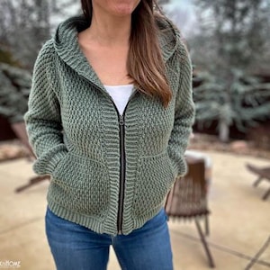 May include: A green hooded sweater with a zipper closure and two pockets. The sweater is made of a textured knit fabric.