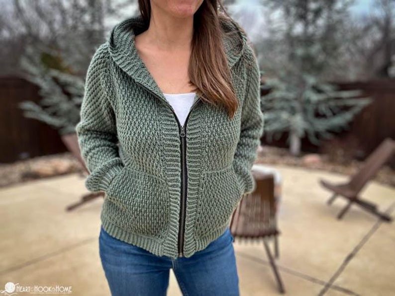 May include: A green hooded sweater with a zipper closure and two pockets. The sweater is made of a textured knit fabric.