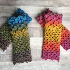 May include: Two pairs of crocheted fingerless gloves with a scale pattern. One pair is blue, green, and brown, and the other is pink, orange, and yellow.