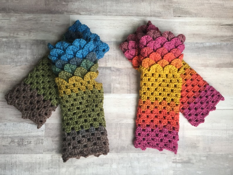 May include: Two pairs of crocheted fingerless gloves with a scale pattern. One pair is blue, green, and brown, and the other is pink, orange, and yellow.