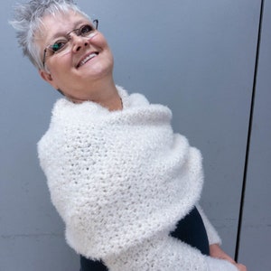 May include: A white crocheted shrug with long sleeves. The shrug is made with a fluffy yarn and has a cowl neck.