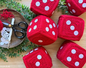 May include: Five large red crocheted dice with white felt dots arranged in various patterns. A wooden bowl contains a ball of red yarn, a pair of black scissors, a white crochet hook, and several small white felt circles for crafting these dice.