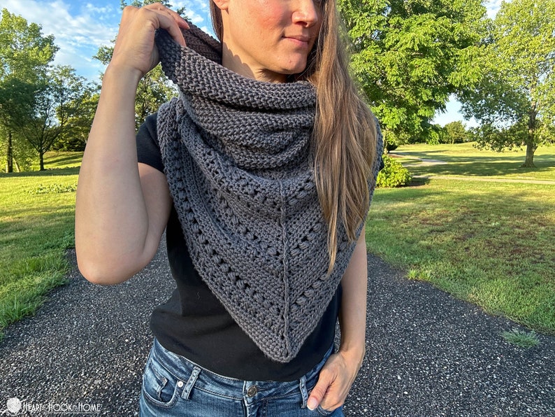 May include: A gray triangular shawl with a lacy pattern and a textured knit. The shawl is worn by a person with long brown hair.