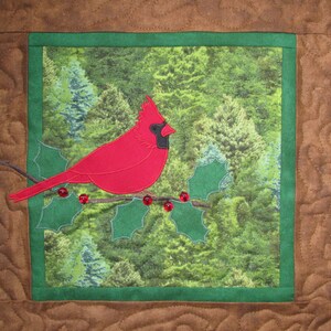 May include: A red cardinal perched on a holly branch with red berries against a green forest background. The cardinal is a popular symbol of Christmas and winter holidays.