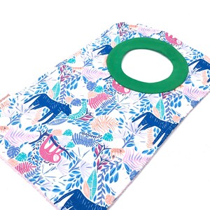 May include: A white baby bib with a green neck opening and a colorful jungle print featuring sloths, leaves, and animals.