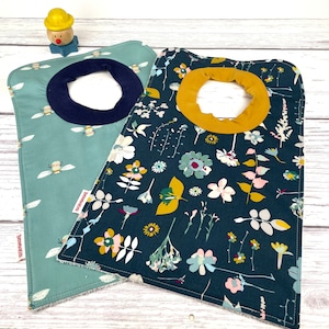 May include: Two fabric baby bibs, one with a blue and green floral pattern and the other with a light blue background and a bee design. The bibs have a yellow trim around the neck.