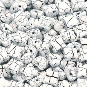 May include: A close-up of a pile of white ceramic beads with black crackle glaze. The beads are all roughly the same size and shape, and they have a slightly irregular surface.