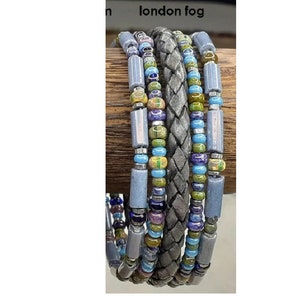 May include: A multi-strand bracelet with grey, blue, green, and purple beads. The bracelet also features a braided leather strap.