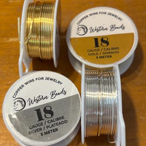 May include: Two spools of 18 gauge copper wire for jewellery making. One spool is gold plated and the other is silver plated. Each spool is labelled "Western Beads" and contains 5 metres of wire.