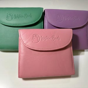 May include: Three small, rectangular, leather pouches with a flap closure. Each pouch is a different color: green, purple, and pink. The pouches have the text "Western Buds" embossed on the front.
