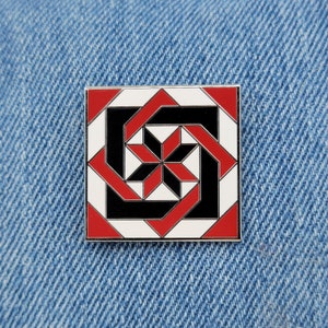May include: A red, white, and black geometric enamel pin with a starburst design. The pin is square shaped and has a silver metal finish.