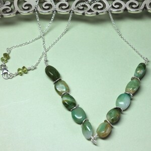 May include: A silver chain necklace with a V-shaped pendant made of green and brown agate stones.