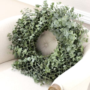May include: A green eucalyptus wreath on a white chair. The wreath is made of fresh eucalyptus leaves and branches.
