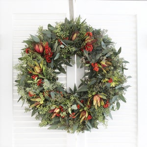 May include: A green, red and brown Christmas wreath with red berries and eucalyptus leaves.