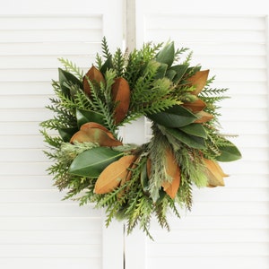 May include: A green and brown wreath made of magnolia leaves and other greenery.