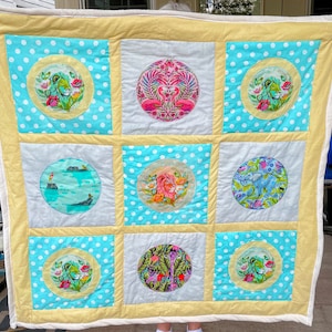 May include: A yellow and blue patchwork quilt with nine squares. Each square has a circular design featuring animals, birds, and plants. The quilt is made with a variety of fabrics and textures.