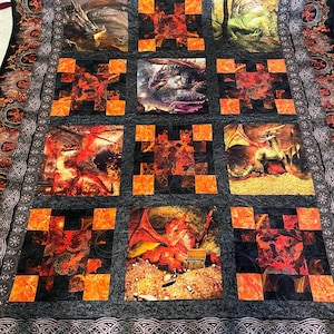 May include: A quilt with a dragon theme. The quilt is made of a dark gray fabric with orange squares. The quilt features nine different images of dragons, some with fire and some with treasure.