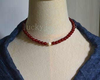 May include: A red beaded necklace with a single white pearl pendant. The necklace is displayed on a mannequin with the text "lucky je" visible.