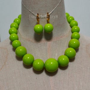 May include: A lime green beaded necklace and matching earrings set. The necklace features large, round beads. The earrings have a similar design, with a single lime green bead suspended from a gold-colored hook. The text "lucky jewelry8" is visible.