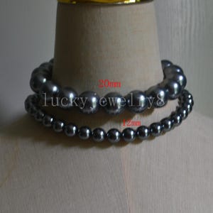 Puede incluir: Dos hilos de collares de perlas grises oscuras. El collar superior tiene perlas de 20 mm, y el collar inferior tiene perlas de 12 mm. El texto "lucky jewellry8" es visible. Los collares se exhiben en un maniquí.