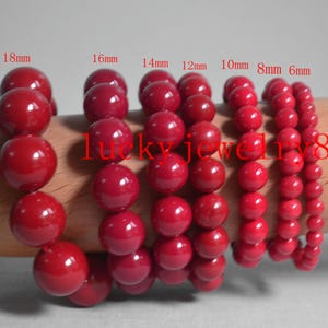 Puede incluir: Se muestran varias pulseras de cuentas rojas con diferentes tamaños de cuentas, de 6 mm a 18 mm. Las pulseras están ensartadas y parecen estar hechas de un material brillante. El texto "lucky jewelry8" es visible.
