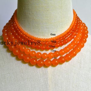 Könnte beinhalten: Mehrere Stränge orangefarbener Edelstein-Perlenketten werden auf einer Schaufensterpuppe präsentiert. Die Perlen variieren in der Größe von 6 mm bis 14 mm. Der Text "Lucky jewelry8" ist auf der linken Seite des Bildes zu sehen.