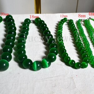 Op de afbeelding: Vijf groene kralenkettingen van verschillende maten. De grootste ketting heeft kralen van 20 mm, gevolgd door 18 mm, 12 mm, 8 mm en 4 mm. De kettingen worden op een wit oppervlak getoond.