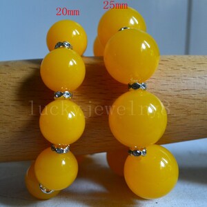May include: Two strands of yellow beaded bracelets. One strand features 20mm beads, the other 25mm beads. Each bead is separated by a silver-coloured spacer. The bracelets are displayed on a wooden surface.