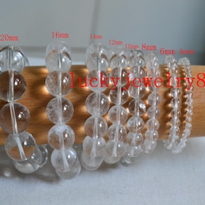 May include: Clear quartz crystal bead bracelets in various sizes, from 4mm to 20mm. The bracelets are displayed on a wooden surface. The text "Lucky jewelry8" is visible.
